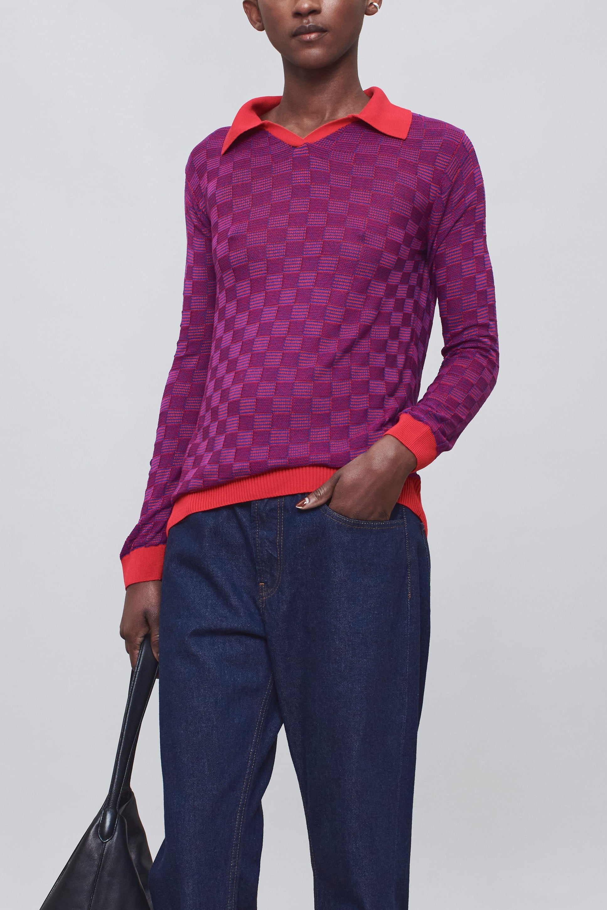 Person wearing a purple patterned top and blue pants, holding a black bag on a white background